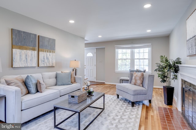 living room featuring recessed lighting, a fireplace with flush hearth, light wood-style flooring, and baseboards