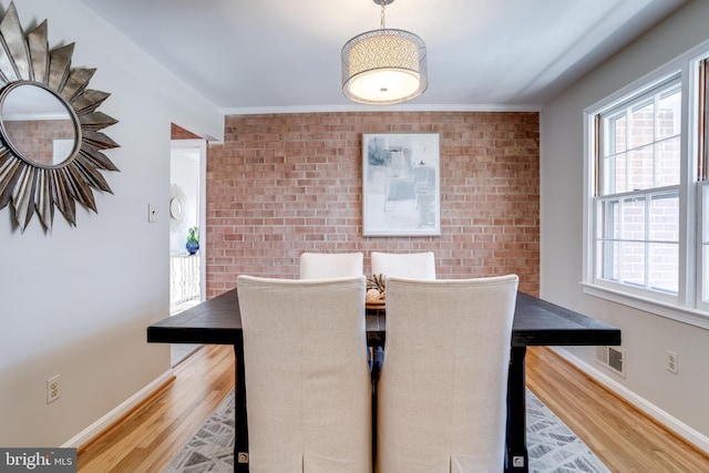 dining space with brick wall, baseboards, an accent wall, and wood finished floors