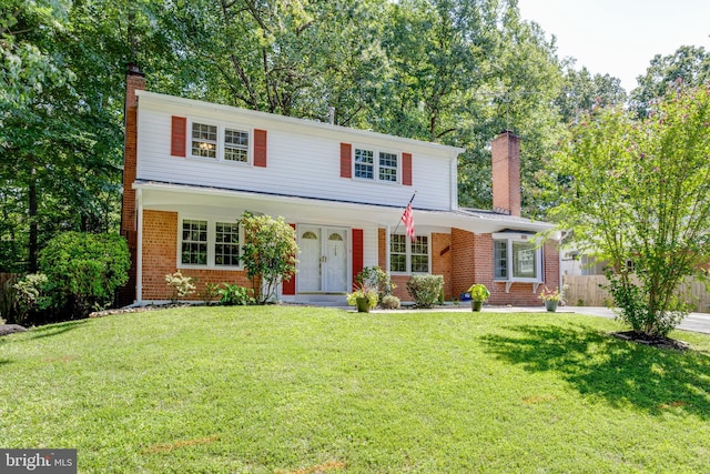 traditional-style house featuring fence, a chimney, a front lawn, and brick siding
