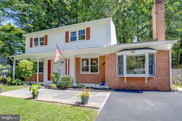 view of front of home featuring a porch, brick siding, fence, and a chimney