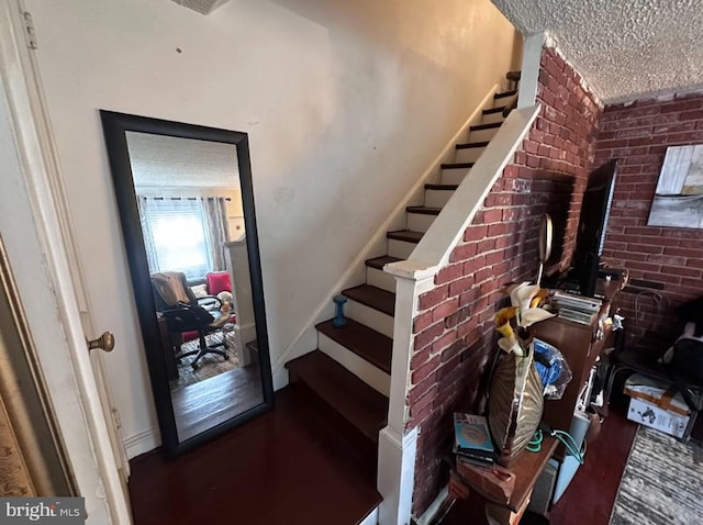 staircase with brick wall and a textured ceiling