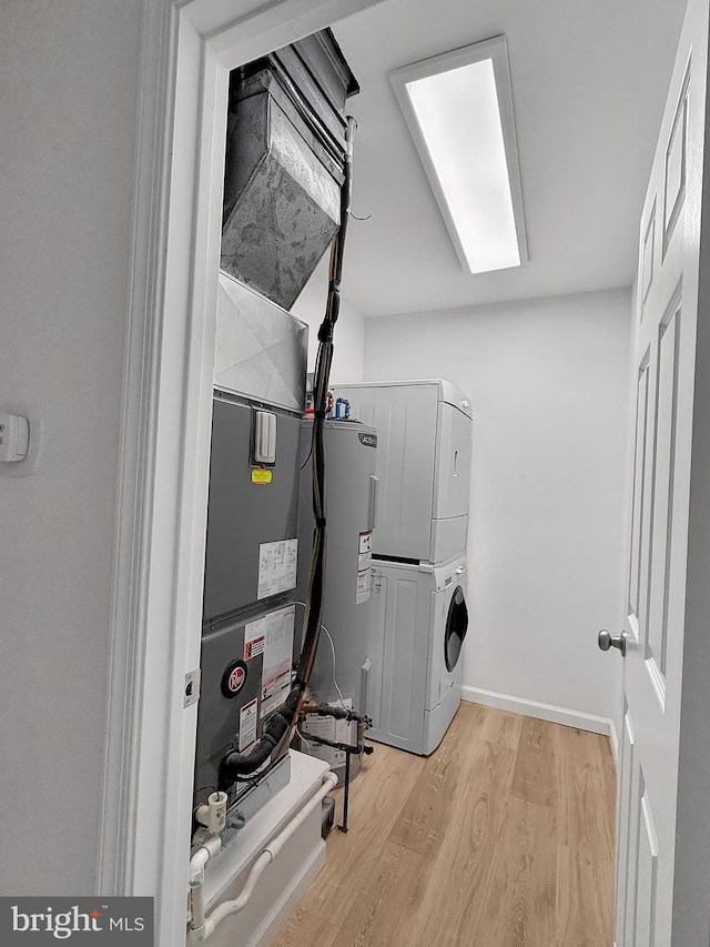 laundry room featuring water heater, stacked washer and clothes dryer, and light wood-type flooring