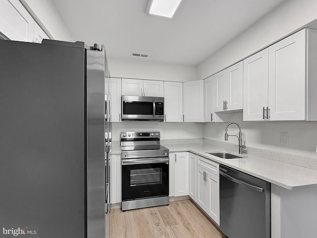 kitchen with light wood-type flooring, stainless steel appliances, sink, and white cabinets