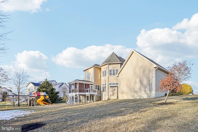 back of house featuring a playground, a sunroom, and a lawn