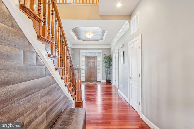 entrance foyer featuring a raised ceiling, ornamental molding, and dark hardwood / wood-style flooring