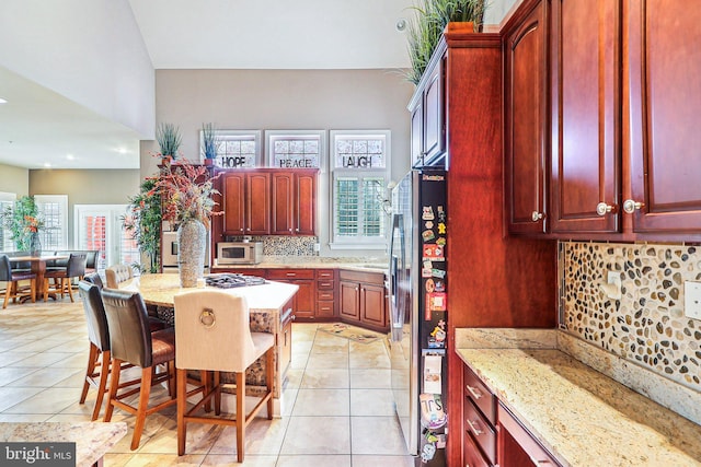 kitchen with appliances with stainless steel finishes, tasteful backsplash, a breakfast bar area, light tile patterned floors, and light stone countertops