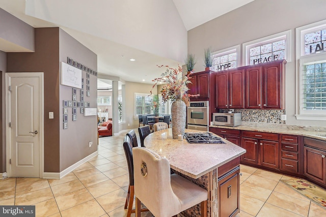 kitchen featuring appliances with stainless steel finishes, a kitchen bar, a center island, light tile patterned floors, and light stone counters