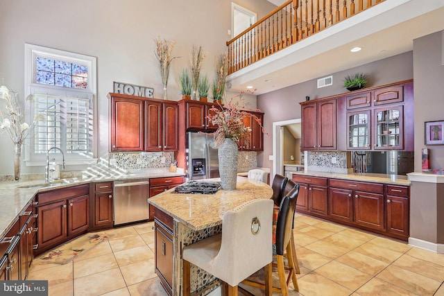 kitchen with a breakfast bar, sink, a kitchen island, stainless steel appliances, and a high ceiling