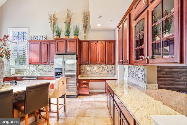 kitchen featuring light stone counters, decorative backsplash, a breakfast bar, and stainless steel refrigerator with ice dispenser