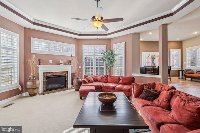 living room with crown molding, ceiling fan, carpet, a high end fireplace, and a raised ceiling