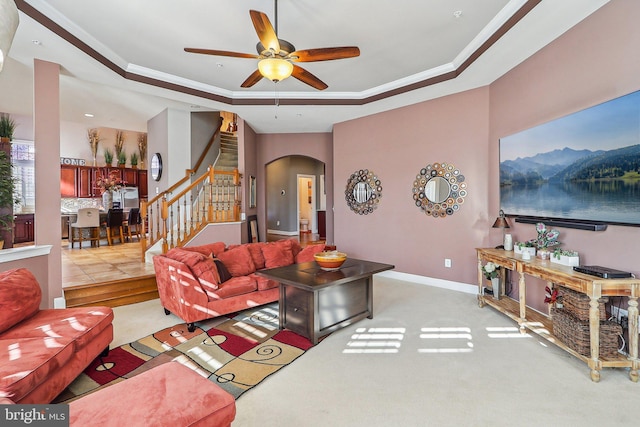 living room featuring ceiling fan, ornamental molding, a tray ceiling, and light carpet