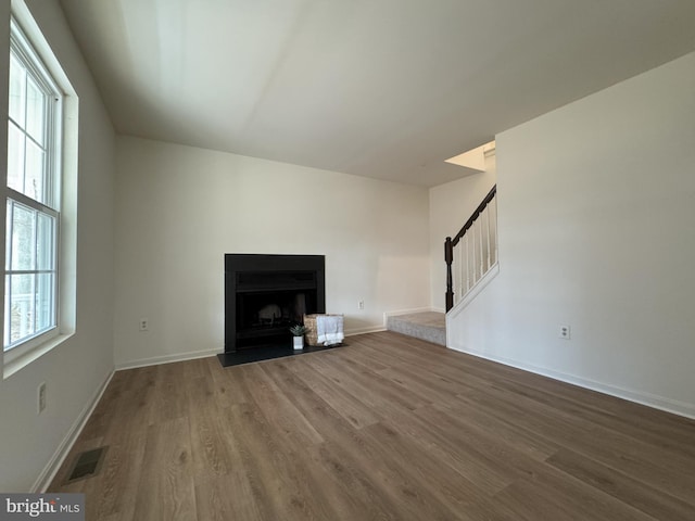 unfurnished living room featuring stairs, plenty of natural light, wood finished floors, and visible vents