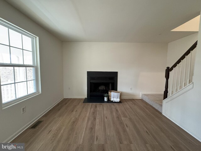 unfurnished living room with a fireplace with flush hearth, visible vents, stairway, and wood finished floors