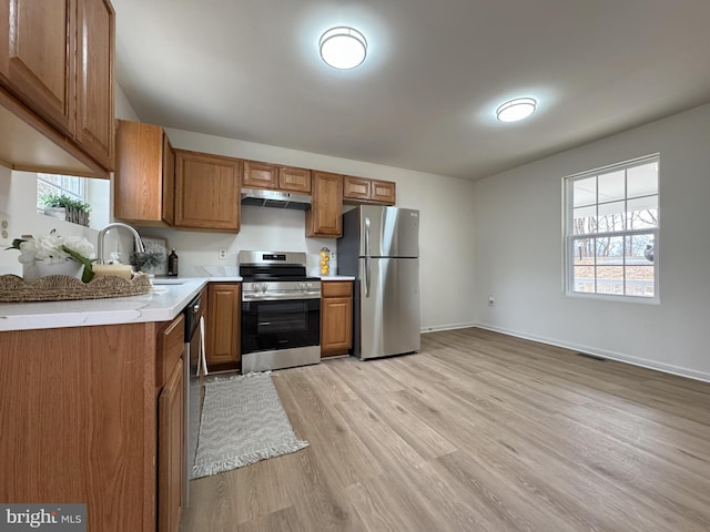 kitchen featuring stainless steel appliances, light countertops, brown cabinetry, a sink, and under cabinet range hood