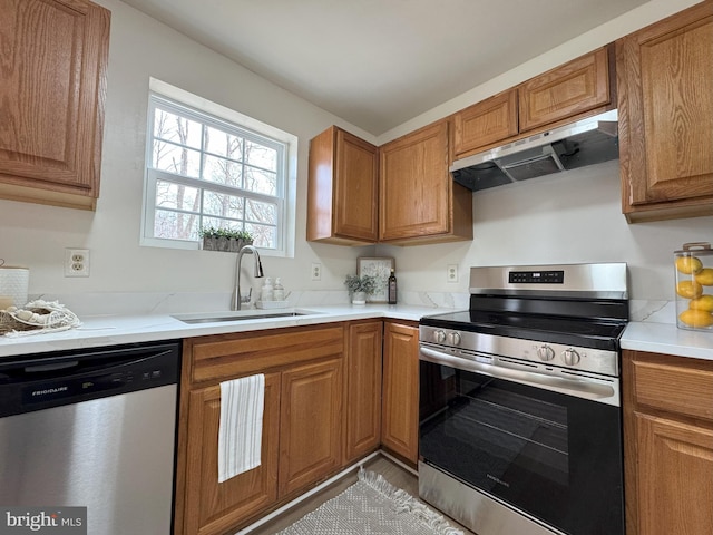 kitchen with under cabinet range hood, appliances with stainless steel finishes, brown cabinets, and a sink