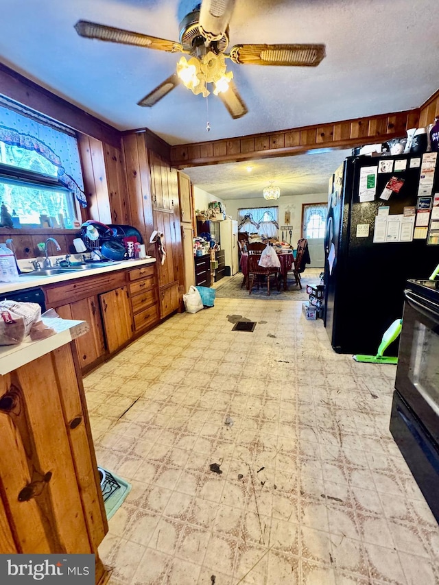 kitchen with sink, black fridge, wooden walls, range with electric cooktop, and ceiling fan