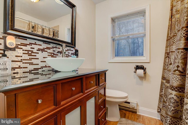 bathroom with toilet, vanity, hardwood / wood-style flooring, decorative backsplash, and a baseboard heating unit