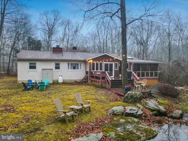 rear view of property featuring an outdoor fire pit, a deck, and a sunroom