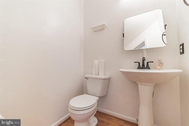 half bathroom with toilet, baseboards, and wood finished floors