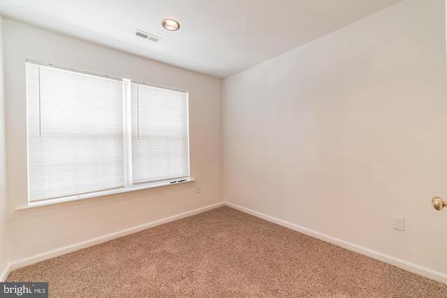 empty room with carpet, visible vents, and baseboards