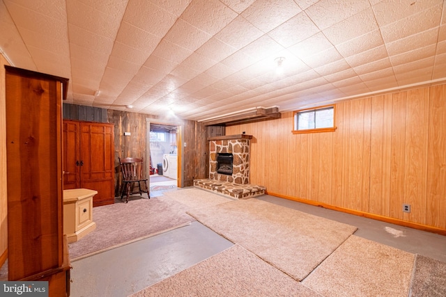 interior space with washer / dryer, wooden walls, light colored carpet, and a stone fireplace