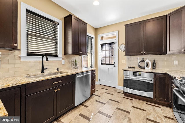 kitchen featuring dark brown cabinetry, appliances with stainless steel finishes, light stone countertops, and sink