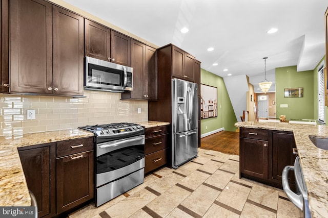 kitchen with hanging light fixtures, stainless steel appliances, light stone counters, tasteful backsplash, and dark brown cabinetry