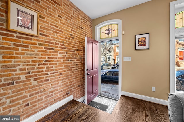 entrance foyer featuring brick wall and dark wood-type flooring