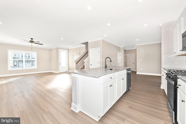 kitchen with sink, appliances with stainless steel finishes, light stone countertops, white cabinets, and a center island with sink