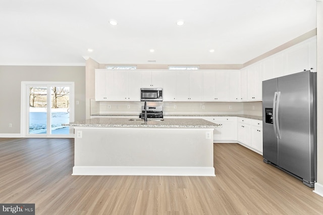 kitchen with appliances with stainless steel finishes, light stone countertops, a kitchen island with sink, and white cabinets