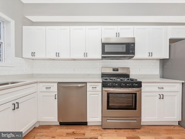 kitchen featuring sink, white cabinetry, stainless steel appliances, tasteful backsplash, and light hardwood / wood-style floors