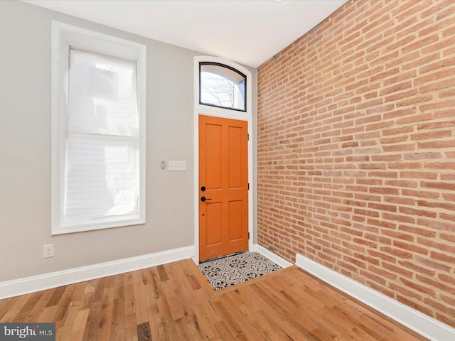 foyer entrance with hardwood / wood-style flooring and brick wall