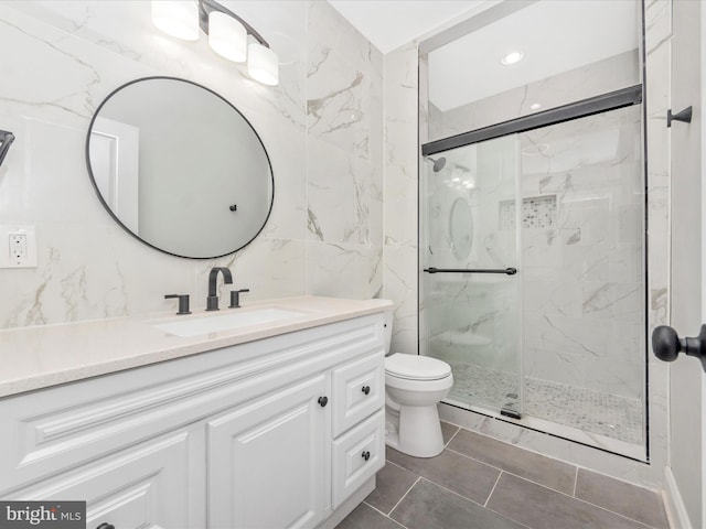 bathroom with tile walls, an enclosed shower, vanity, and toilet