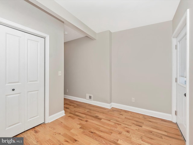 unfurnished bedroom featuring beam ceiling, light hardwood / wood-style floors, and a closet