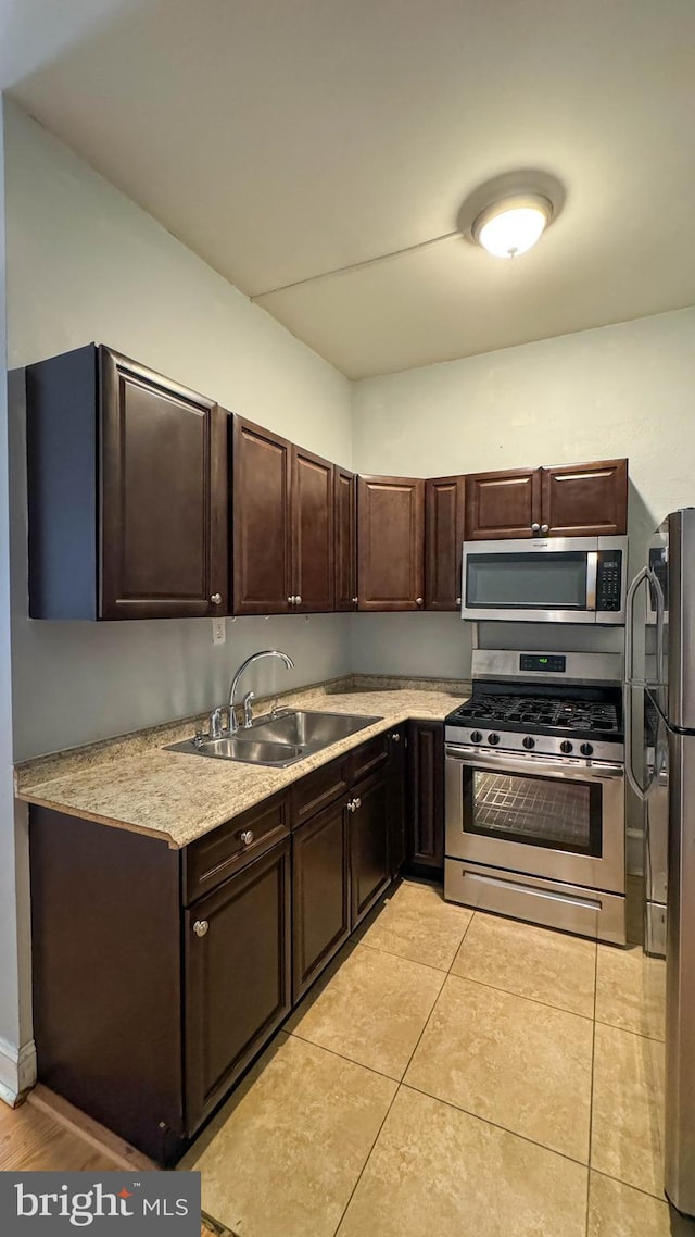 kitchen featuring appliances with stainless steel finishes, sink, dark brown cabinets, and light tile patterned floors