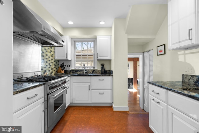 kitchen with white cabinets, backsplash, stainless steel stove, wall chimney range hood, and a sink