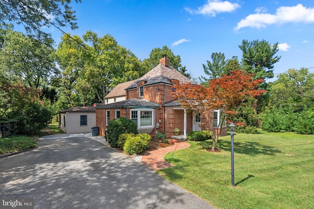 view of front of house featuring brick siding, driveway, a chimney, and a front lawn