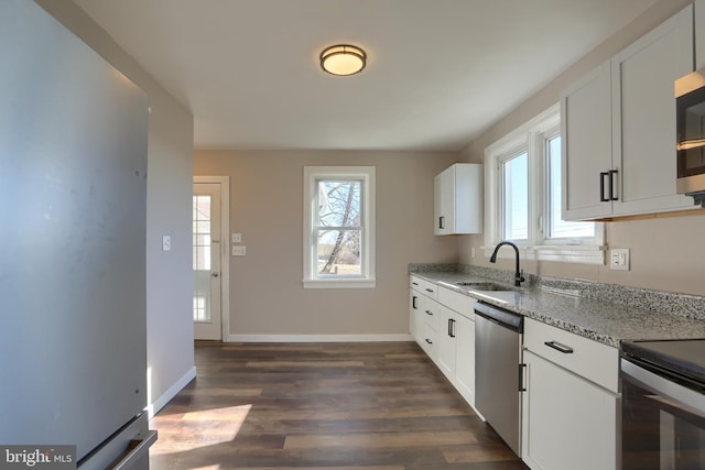 kitchen with sink, appliances with stainless steel finishes, light stone counters, a healthy amount of sunlight, and white cabinets