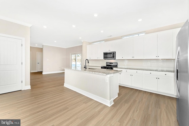 kitchen featuring stainless steel appliances, an island with sink, light stone countertops, and white cabinetry