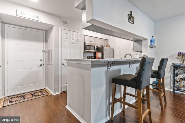 kitchen featuring dark wood-type flooring, a kitchen bar, kitchen peninsula, stainless steel appliances, and white cabinets