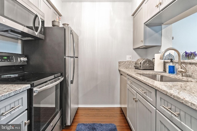 kitchen featuring sink, appliances with stainless steel finishes, gray cabinetry, dark hardwood / wood-style floors, and light stone counters