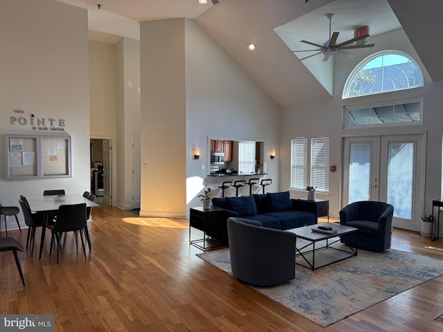 living room featuring a high ceiling, ceiling fan, light wood-type flooring, and french doors