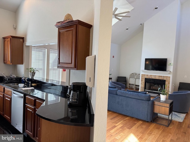 kitchen featuring ceiling fan, dishwasher, high vaulted ceiling, a fireplace, and light hardwood / wood-style floors