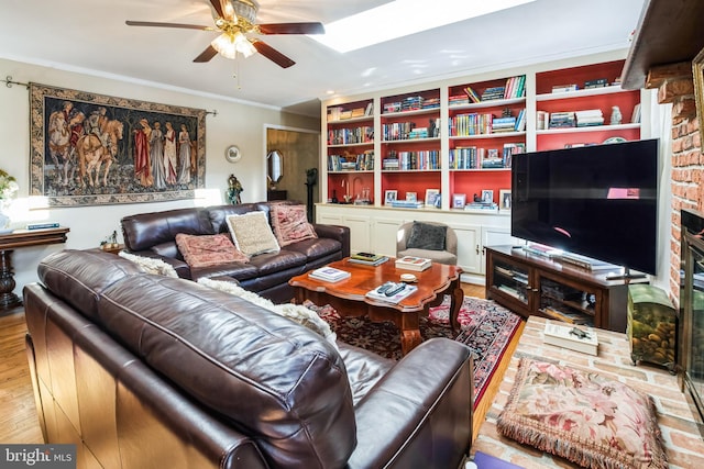 living room featuring built in shelves, ornamental molding, ceiling fan, and light wood-type flooring