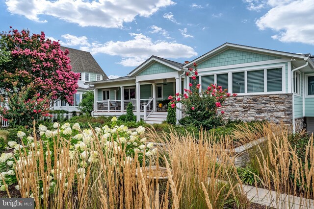 view of front facade featuring stone siding, covered porch, and fence