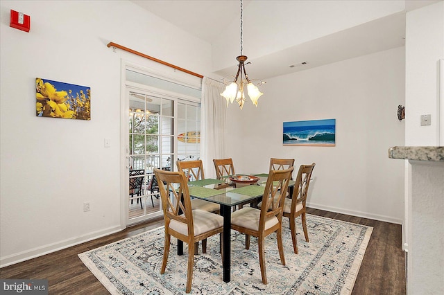 dining area with dark wood-type flooring and an inviting chandelier