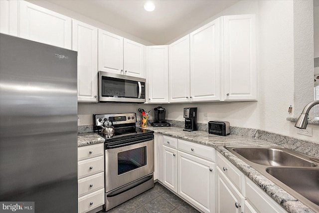 kitchen with white cabinetry, stainless steel appliances, sink, and dark tile patterned floors