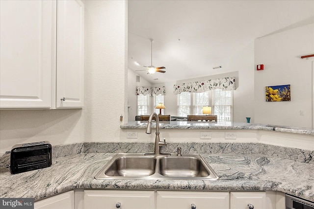 kitchen with lofted ceiling, sink, white cabinets, light stone counters, and ceiling fan