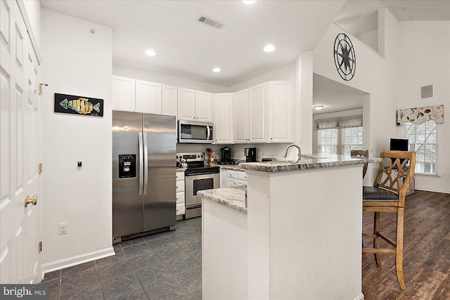 kitchen with appliances with stainless steel finishes, white cabinetry, a kitchen breakfast bar, light stone counters, and kitchen peninsula