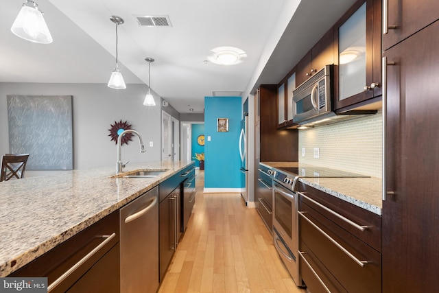 kitchen featuring sink, light hardwood / wood-style flooring, backsplash, stainless steel appliances, and light stone counters